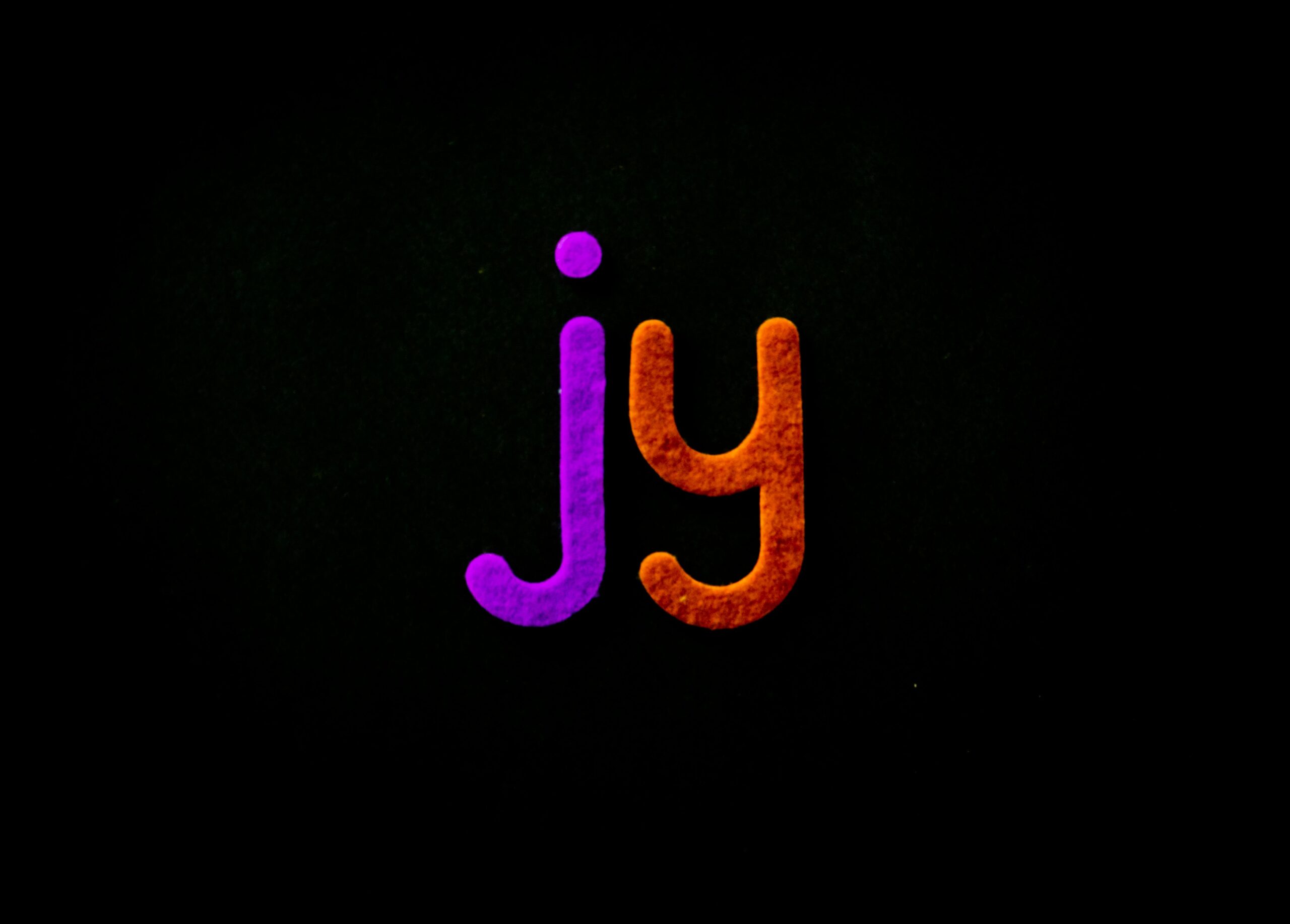 Bright and colorful letters 'jy' pop against a black background, creating a striking visual contrast.